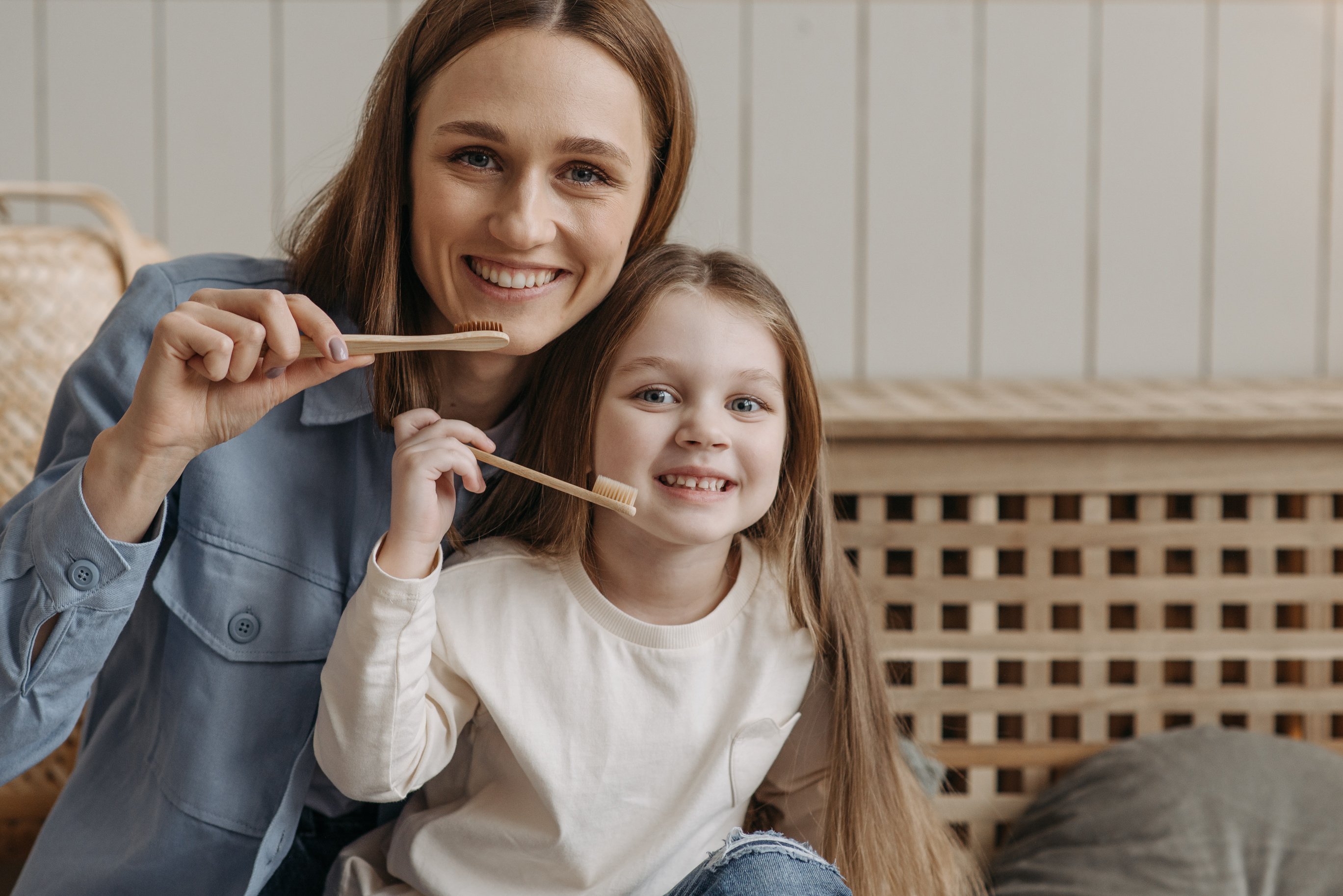 A Woman and a Child Smiling While Holding a Wooden Toothbrush